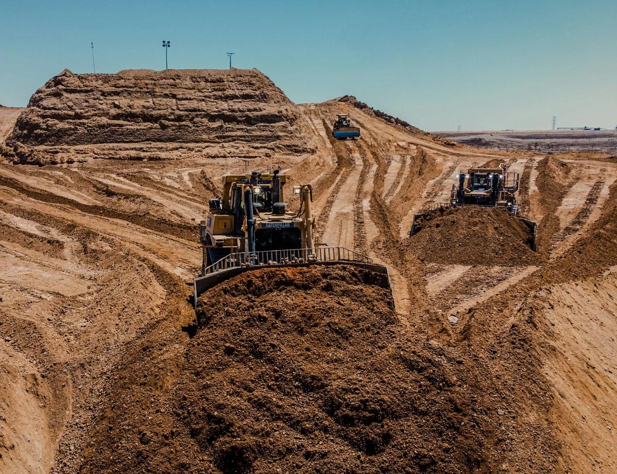 Autonomous Caterpillar dozers and a grader working a large earthmoving site, seen from above.