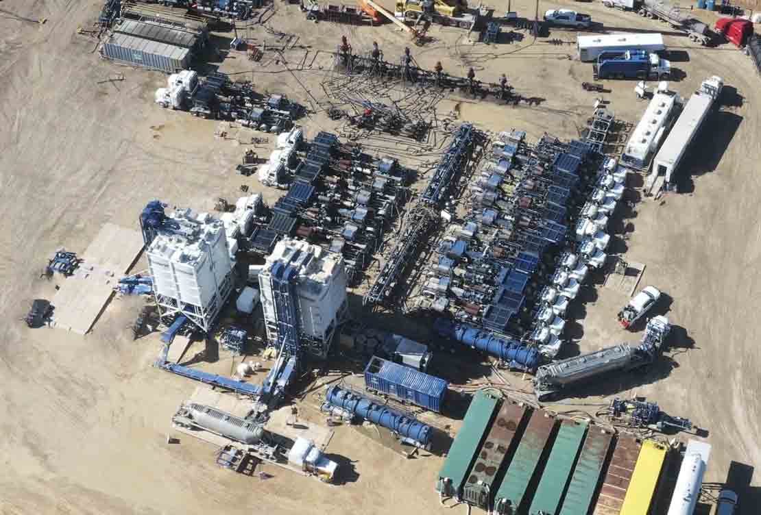 Aerial view of a stimulation site: rows of pump units, blenders and manifold trailers laid out around a wellhead.