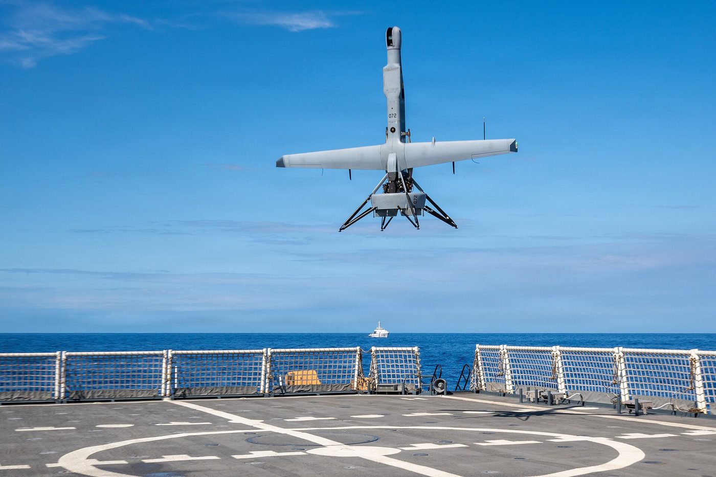 A V-BAT uncrewed aircraft hovering above a ship's flight deck at sea before landing.